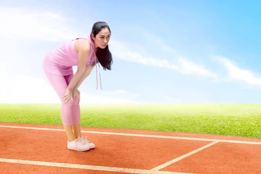 Asian runner woman take a break after running on the running track with a blue sky background
