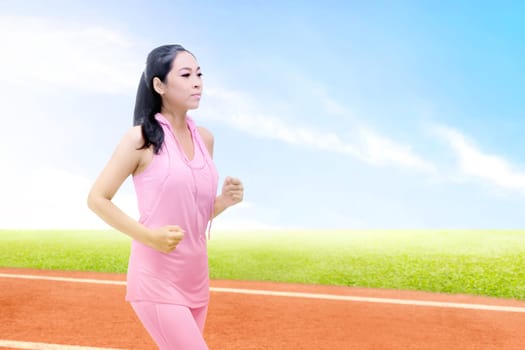 Asian runner woman running on the running track with a blue sky background
