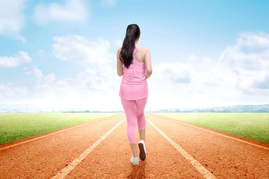 Rear view of Asian runner woman running on the running track with a blue sky background