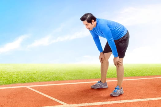 Asian runner man take a break after running on the running track with a blue sky background