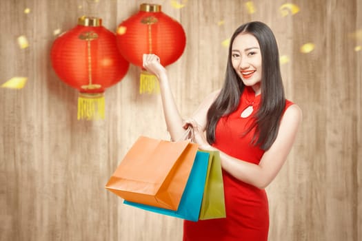 Asian Chinese woman in cheongsam dress holding shopping bags. Happy Chinese New Year