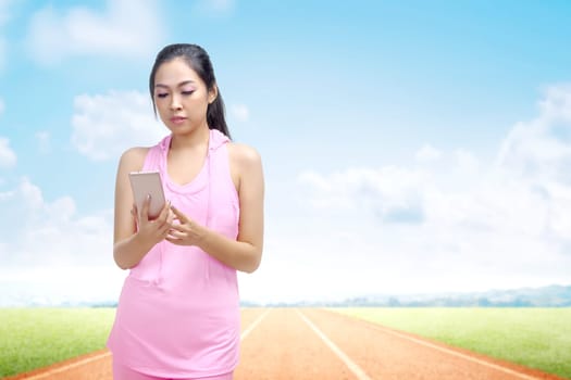Asian runner woman using a mobile phone at the break after running on the running track with a blue sky background