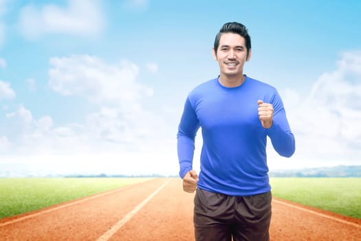 Asian runner man running on the running track with a blue sky background