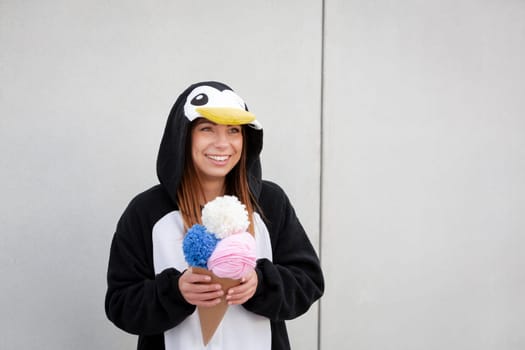 beautiful, young woman in penguin costume is eating decoration ice cream in front of concrete wall