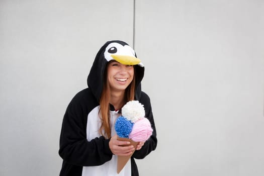 beautiful, young woman in penguin costume is eating decoration ice cream in front of concrete wall