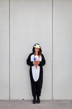 beautiful, young woman in penguin costume is eating decoration ice cream in front of concrete wall
