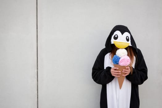 beautiful, young woman in penguin costume is eating decoration ice cream in front of concrete wall