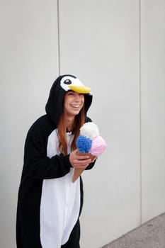 beautiful, young woman in penguin costume is eating decoration ice cream in front of concrete wall