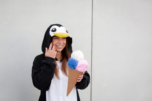 beautiful, young woman in penguin costume is eating decoration ice cream in front of concrete wall