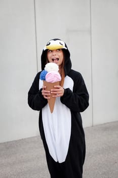 beautiful, young woman in penguin costume is eating decoration ice cream in front of concrete wall