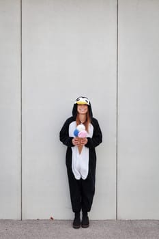 beautiful, young woman in penguin costume is eating decoration ice cream in front of concrete wall