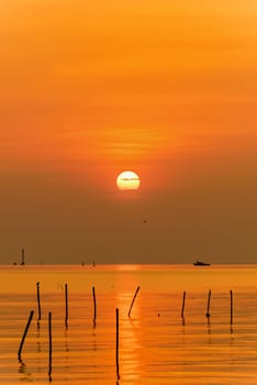 Beautiful nature landscape bright yellow sun reflecting orange light on the water surface of the sea and golden sunlight in sky, Colorful sunset at the tropical coast in Bangpu, Samut Prakan, Thailand