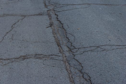 Asphalt road surface with small cracks and damages. Sidewalk asphalt road with cracks. Floor. Texture of tarmac road with cracks. Abstract background