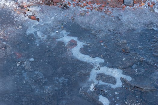 Frozen Puddle with broken ice. Ice Crust On Frozen Puddle. Winter background. Frozen puddle on the road. In January. Frozen Puddle And Dirt Road Close-Up.