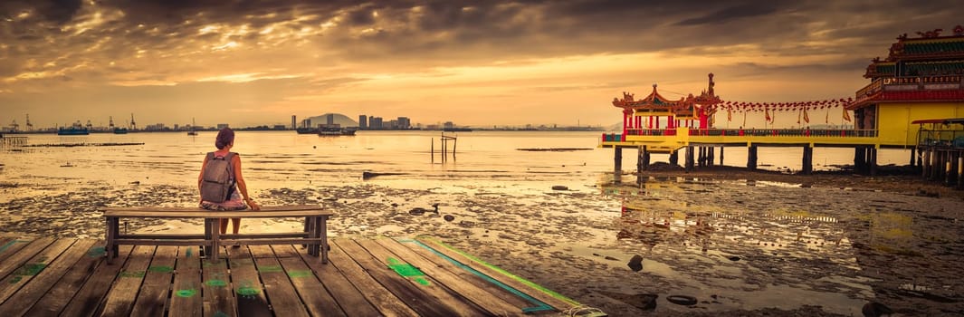 Tourist sitting at Yeoh jetty at sunrise, Georgetown, Penang, Malaysia. Panorama