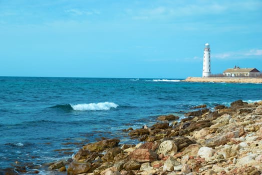 Old lighthouse on the sea coast. Storm, waves and blue sky.