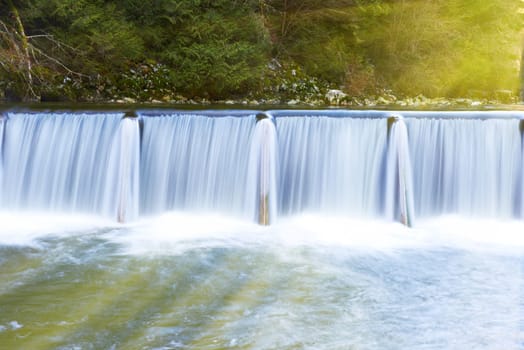 Sunny waterfall cascade streaming down in the green forest