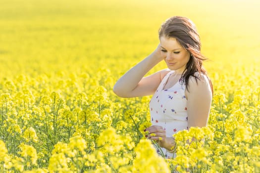Beautiful girl eyes closed in yellow flowers field infinite horizon. Sunny sun sunshine and authentic lifestyle in windy weather hair.