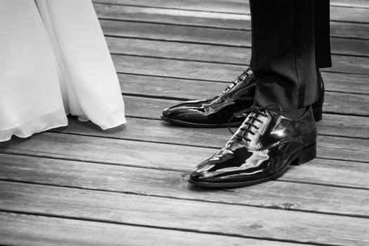 The man and the woman wearing luxury lifestyle bridal dress, suit and shoes. The Male shoe luster is polished. Wooden floor copyspace.