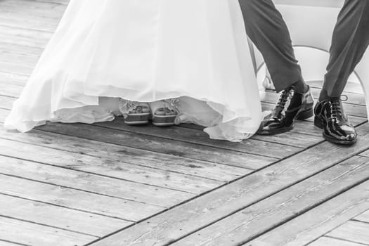 The man and the woman wearing luxury bridal dress, suit and shoes. The girl shows her feet with nail varnish. Male shoe is polished.