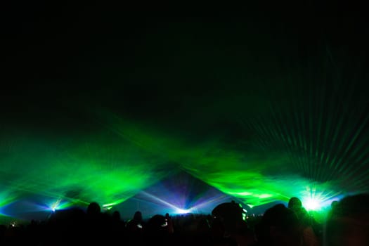 Luxury entertainment with audience silhouettes in nightclub event, festival or New Year's Eve. Beams and rays shining colorful lights.