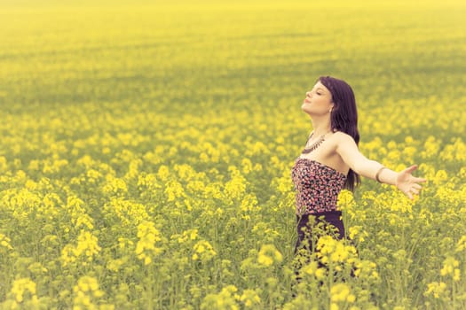 Attractive young beauty girl enjoying the warm sunny sun in nature rapeseed field takes time feeling sustainability and contemplation.