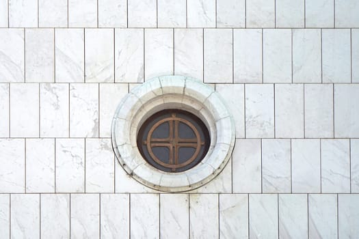 Round window at white marble wall of church
