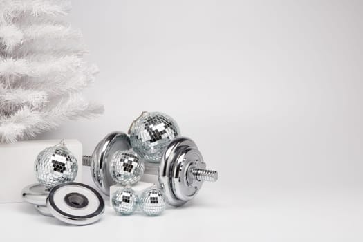 Dumbbells, Christmas fir tree and mirorr balls on white background with copy space. For design of advertising, web design. Christmas and New Year. Fitness, sport or healthy lifestyle concept.