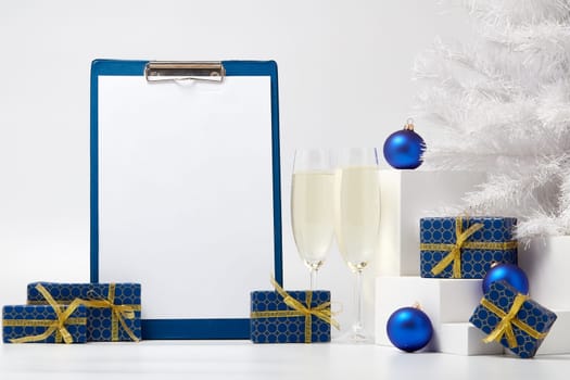 Gift boxes, blank clipboard, two champagne flutes, fir tree and Christmas decoration on white background with copy space. Christmas and New Year. For advertising. Greeting card. Winter sale