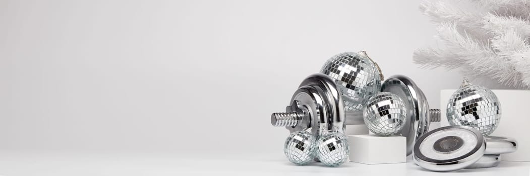 Dumbbells, Christmas fir tree and mirorr balls on white background with copy space. For design of advertising, web design. Christmas and New Year. Fitness, sport or healthy lifestyle concept.