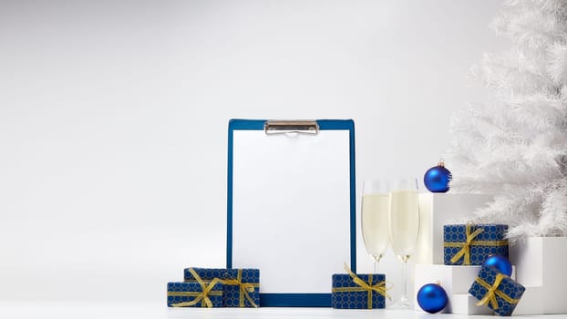 Gift boxes, blank clipboard, two champagne flutes, fir tree and Christmas decoration on white background with copy space. Christmas and New Year. For advertising. Greeting card. Winter sale