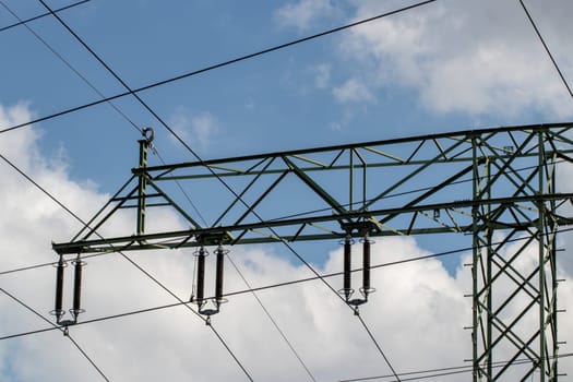 Power generation, transmission and distribution concept. Close-up of a electricity supply pylon and the high voltage power lines against a blue cloudy sky. Facilities for the transmission of electrical energy. Macro.