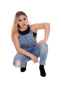 A lovely young blond woman in working jeans crouching on the floor.in the studio, isolated for white background.