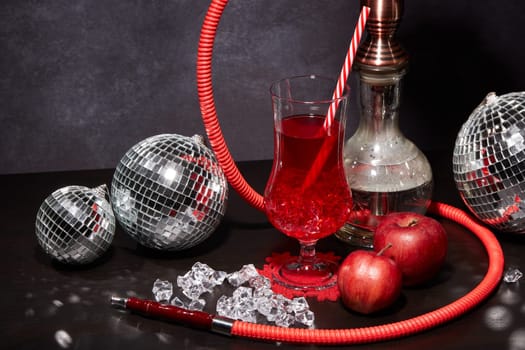 Hookah (shisha), mirror balls (disco ball), glass with cocktail, red apples and ice on dark grey background. New Year and Christmas. Weekend or holiday party