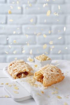 Almond flakes falling from above over caramel strudel on white brick background