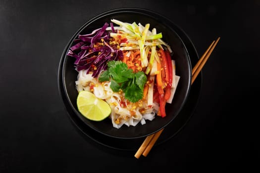 Spicy rice noodel salad in a black bowl with chopsticks, including peppers, cabbage, scallions, and chili lime dressing