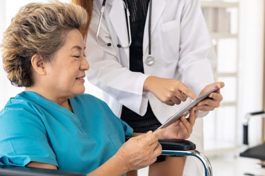 Asian confidence doctor using digital tablet expressing health concerns with old elderly woman patient sit on wheelchair