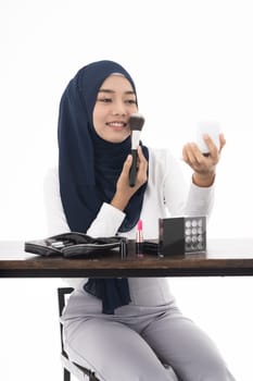 Young Muslim woman do face cosmetic with mirror and makeup brush on white background taken in studio. Using for Fashion and beauty concept