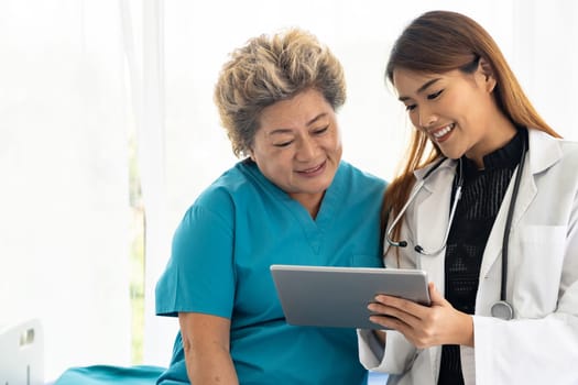 Asian confidence doctor using digital tablet expressing health concerns with old elderly woman patient sit on bed