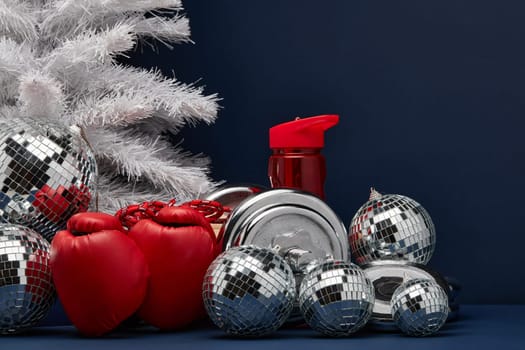 Dumbbell, boxing gloves, skipping rope, Christmas decoration on dark blue background with copy space. For design of advertising, web design. Christmas and New Year. Fitness, sport or healthy lifestyle