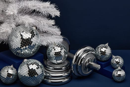 Dumbbells, Christmas fir tree and mirorr balls on dark blue background with copy space. For design of advertising, web design. Christmas and New Year. Fitness, sport or healthy lifestyle concept.