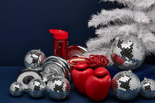 Dumbbell, boxing gloves, skipping rope, Christmas decoration on dark blue background with copy space. For design of advertising, web design. Christmas and New Year. Fitness, sport or healthy lifestyle