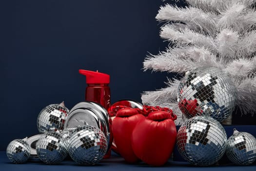 Dumbbell, boxing gloves, skipping rope, Christmas decoration on dark blue background with copy space. For design of advertising, web design. Christmas and New Year. Fitness, sport or healthy lifestyle