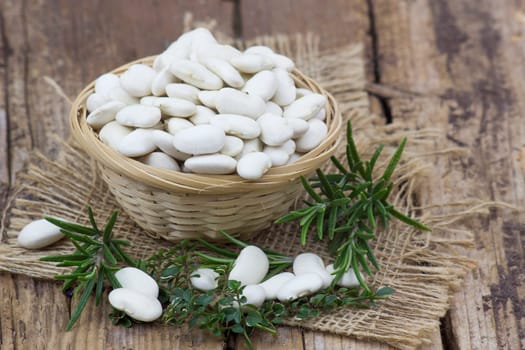 white beans and herbs in a basket on wooden background