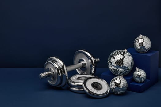 Dumbbell with weights and mirorr balls on dark blue background with copy space. For design of advertising, web design. Christmas and New Year. Fitness, sport or healthy lifestyle concept.
