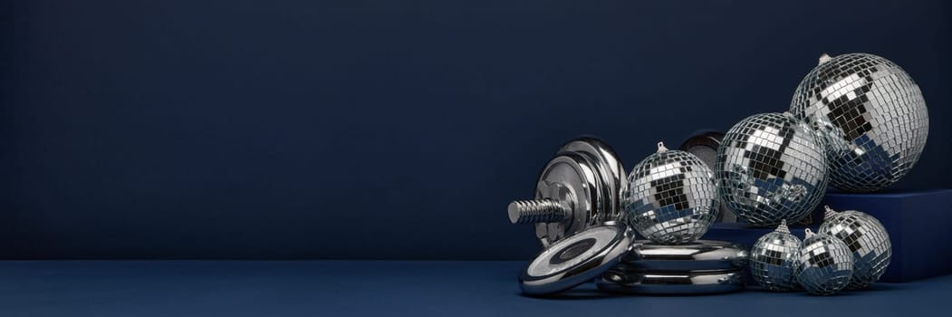Dumbbell with weights and mirorr balls on dark blue background with copy space. For design of advertising, web design. Christmas and New Year. Fitness, sport or healthy lifestyle concept.