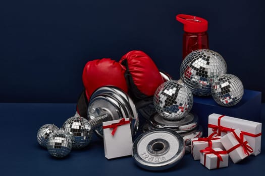 Dumbbell, boxing gloves, gift boxes and mirorr balls on dark blue background with copy space. For design of advertising, web design. Christmas and New Year. Fitness, sport or healthy lifestyle concept