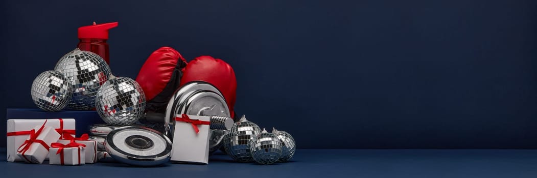 Dumbbell, boxing gloves, gift boxes and mirorr balls on dark blue background with copy space. For design of advertising, web design. Christmas and New Year. Fitness, sport or healthy lifestyle concept