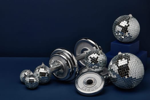 Dumbbell with weights and mirorr balls on dark blue background with copy space. For design of advertising, web design. Christmas and New Year. Fitness, sport or healthy lifestyle concept.