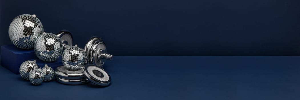Dumbbell with weights and mirorr balls on dark blue background with copy space. For design of advertising, web design. Christmas and New Year. Fitness, sport or healthy lifestyle concept.